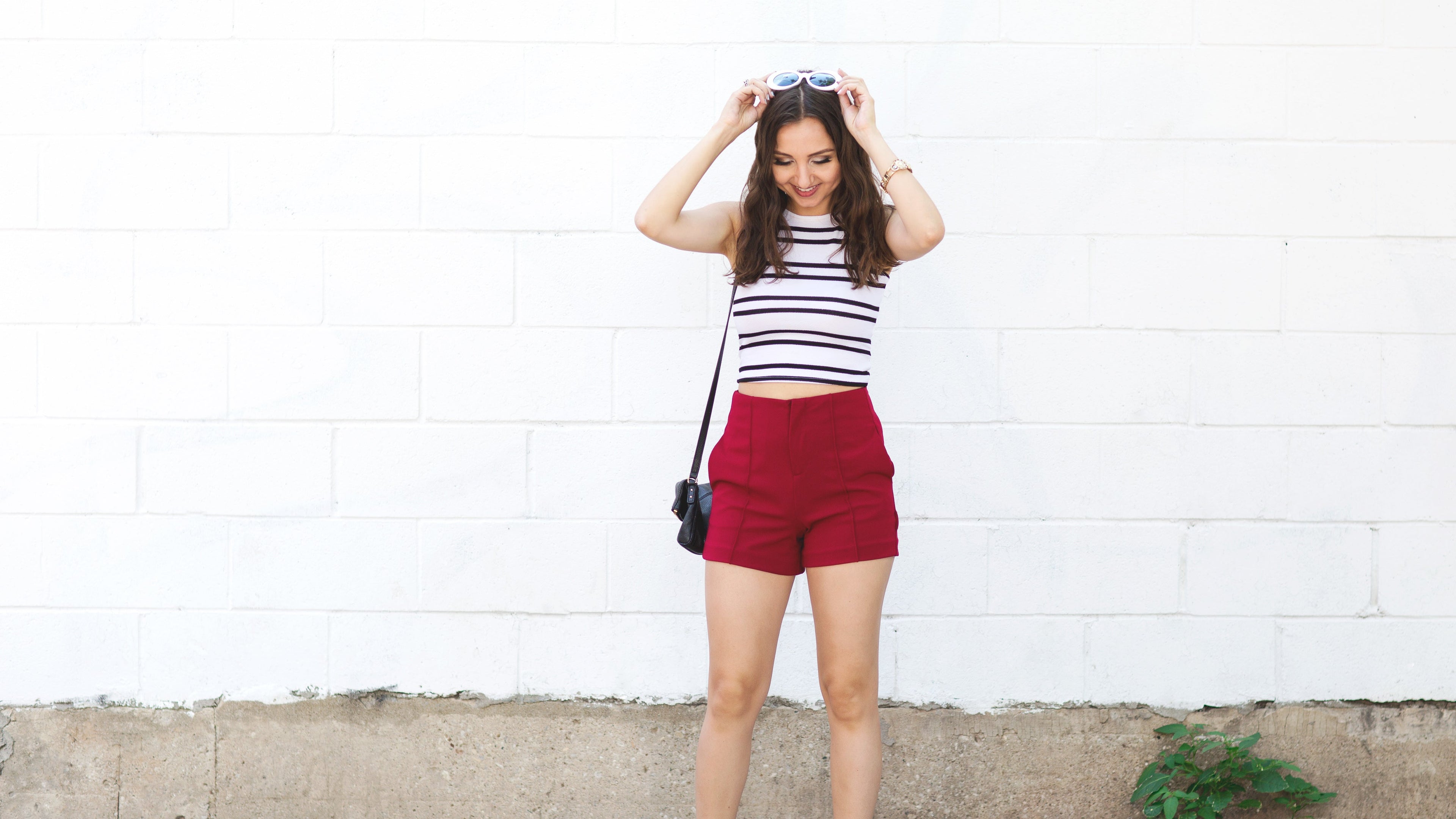 Woman wearing a striped top and red shorts standing against a white wall.